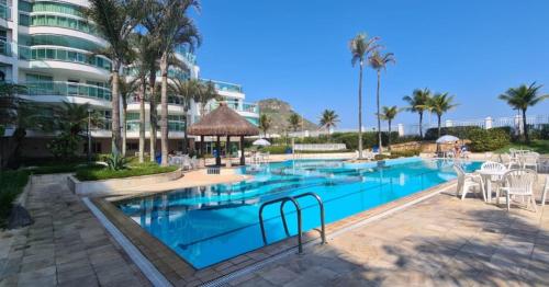 una piscina con mesas y sillas y un edificio en Maravilhoso flat em Pontal Beach Resort Recreio RJ, en Río de Janeiro