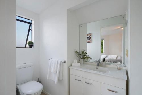 a white bathroom with a toilet and a sink at Elegant 2BR Family Home - Aircon - 5min to Beach in Auckland