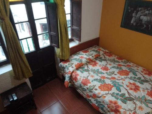 a bedroom with a bed with a floral comforter and windows at Hotel El Dorado La Candelaria in Bogotá