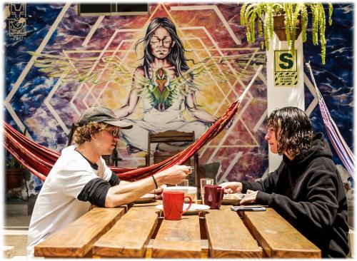 Dois homens sentados numa mesa em frente a um quadro. em ATMA Hostel & Yoga em Huanchaco