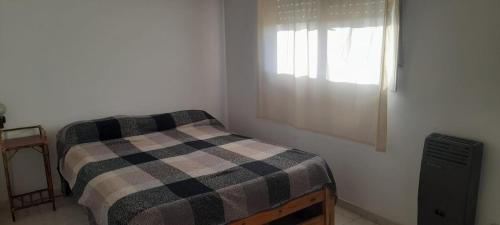 a bedroom with a bed with a checkered blanket and a window at DptosECONOMICOS2 in Necochea