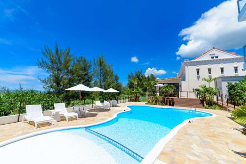 a swimming pool with chairs and umbrellas next to a house at Best Western Okinawa Onna Beach in Onna