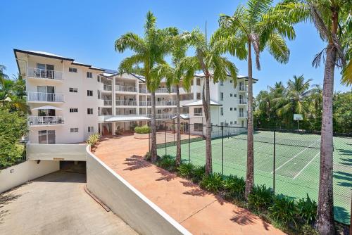 an apartment building with a tennis court and palm trees at Golden Sands Beachfront Resort in Yorkeys Knob