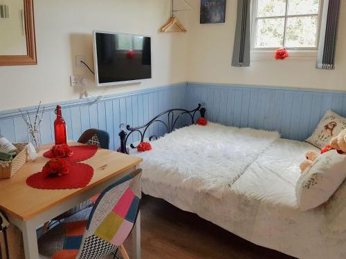 een slaapkamer met een bed en een tafel en een televisie bij The Shepherds Hut in Herstmonceux