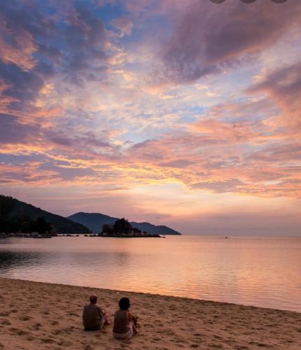 two people sitting on the beach watching the sunset at Batu Ferringhi Luxury Seaview Suite - 3Br in Batu Ferringhi