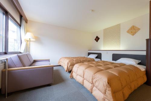 a bedroom with two beds and a couch and a window at Shiga Kogen Olympic Hotel in Yamanouchi