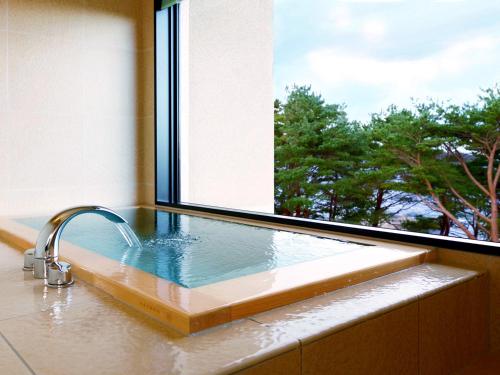 a bath tub with a window and a sink at Jodogahama Park Hotel in Miyako