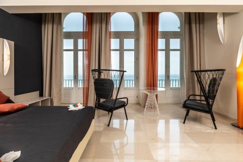 a bedroom with a bed and two chairs and windows at Central Gallery Rooms- Palazzo D'Ali' Staiti XIX in Trapani