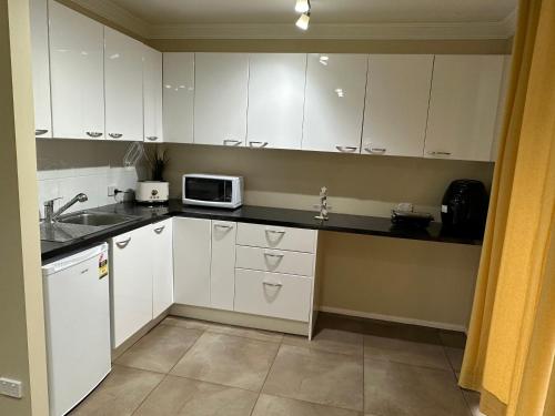 a kitchen with white cabinets and a microwave at One bedroom studio in North Tamborine