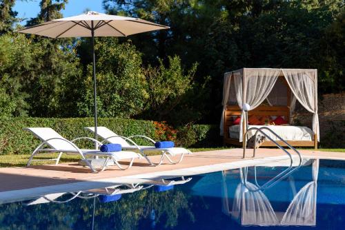 a pool with chairs and an umbrella and a bed at Kallithea Breeze Luxury Villa in Koskinou