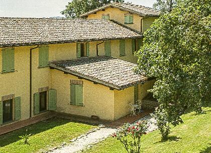 a yellow house with green windows and a yard at Abadia Farneto in Gubbio