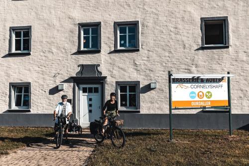 two people on bikes in front of a building at Hotel Cornelyshaff in Heinerscheid