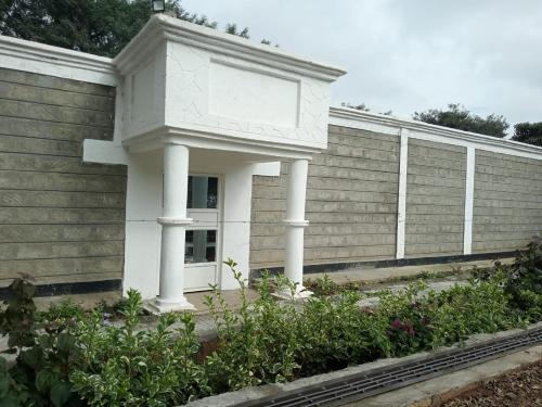 a white building with columns in front of a wall at Brooks Lodge in Nakuru
