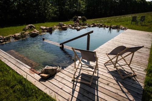 two chairs sitting on a wooden deck with a pond at Usedlost U lípy Blatiny in Sněžné
