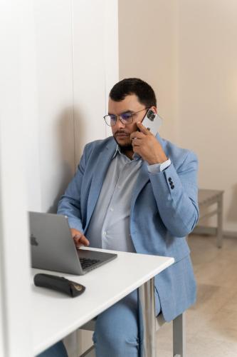 a man sitting at a table with a laptop and talking on a cell phone at Alpha Studios Naxos - Adults Only in Naxos Chora
