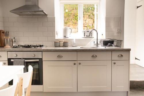 cocina con armarios blancos, fregadero y ventana en Charming 2BD Cottage wIth beautiful views nr Bath en Batheaston