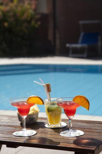 three cocktails on a table next to a swimming pool at Hotel Venezia in Marina di Pietrasanta