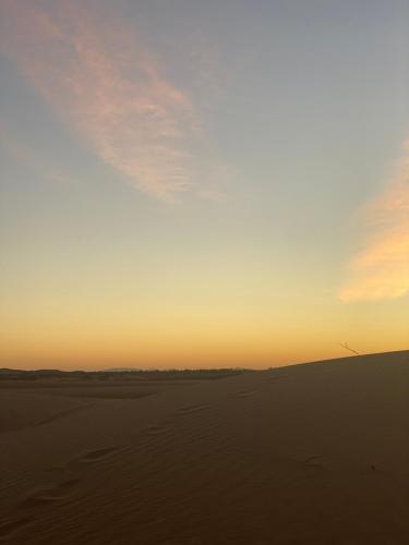 a sunset in the desert with a windmill in the distance at Merzouga Luxury Tents - Glamping in Merzouga