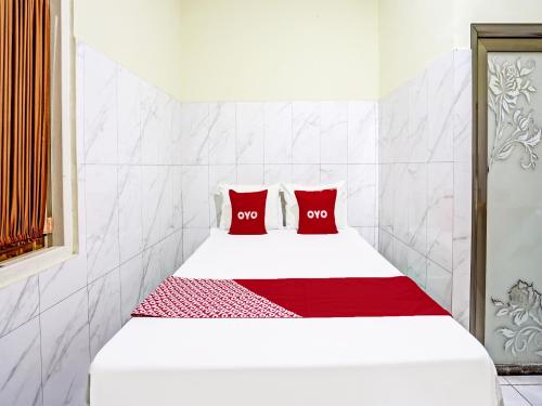 Una cama blanca con dos almohadas rojas. en OYO Life 91884 Kost Kusuma Dewi Syariah, en Sidoarjo