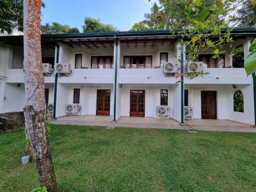 a white building with red doors and a grass yard at Villa Birdlake in Hikkaduwa