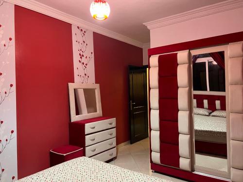 1 dormitorio con paredes rojas, 1 cama y espejo en Appartement Tanger familles, en Tánger
