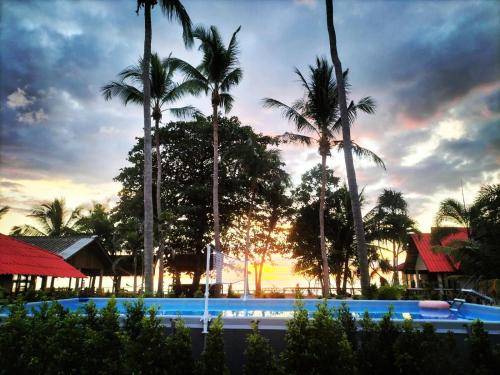 a pool with palm trees and a sunset in the background at Lanta Beach Resort in Ko Lanta