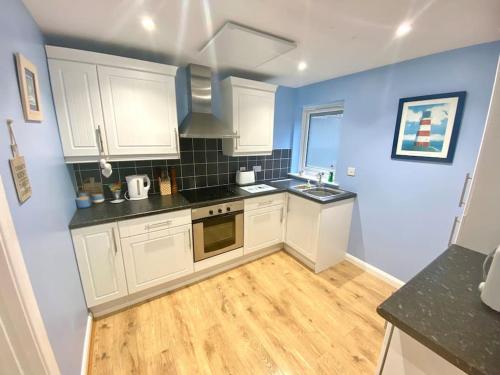 a kitchen with white cabinets and a wooden floor at Modern Spacious Annex -Ground Floor in Brightlingsea