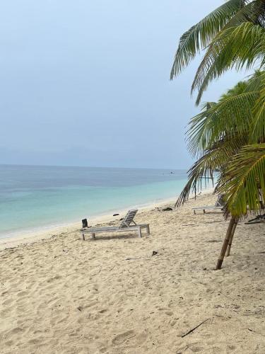 a beach with two lounge chairs and a palm tree at Chekesh Casa in Siquijor