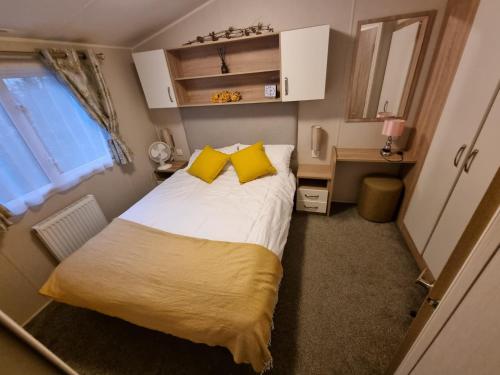 um pequeno quarto com uma cama grande e almofadas amarelas em The Beeches Holiday Home- based at Aberdunant Hall Holiday Park em Prenteg