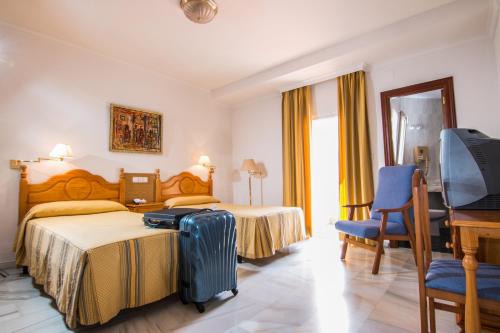 a hotel room with a bed with a suitcase and a desk at Hotel Abades Loja in Loja