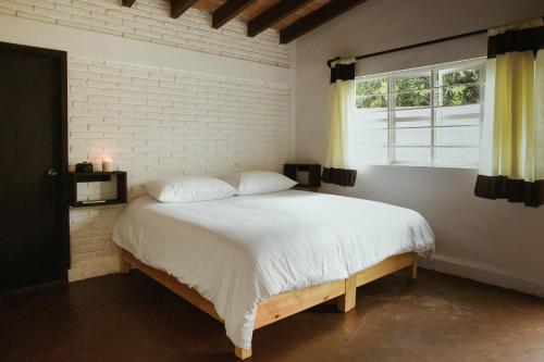 1 dormitorio con 1 cama blanca grande y ventana en Hospedaje Temazcaltitla, en Tepoztlán