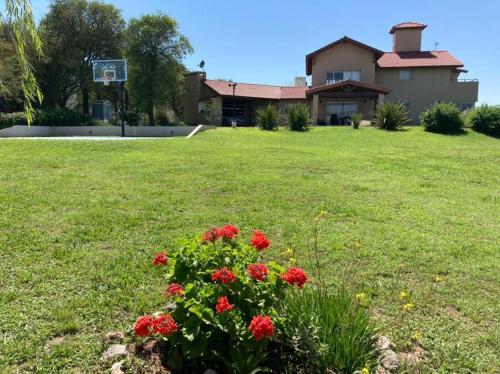 a house with a lawn with red flowers in the yard at Casa con vista a las sierras de Cordoba in Malagueño
