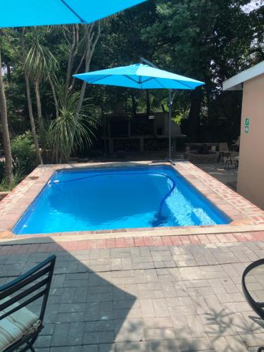 a blue swimming pool with an umbrella and a patio at JC Studios Ermelo in Ermelo