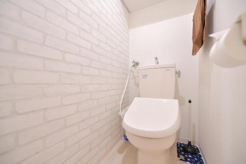 a bathroom with a toilet with a white brick wall at GLASS Yamahana EAST in Minami-jūichijō
