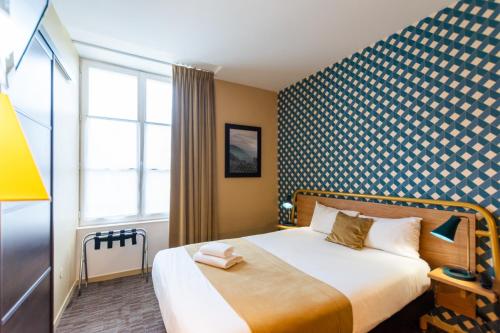 a bedroom with a bed with a blue and white patterned wall at Logis Hôtel Le Vert Galant in La Flèche