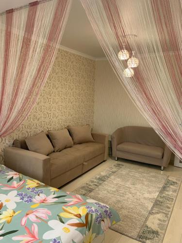 sala de estar con sofá, cama y cortinas en 1 комнатная квартира, en Astana