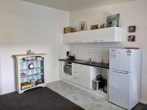 Home Away from Home - Waitaki Lakes Apartment A5 في Otematata: مطبخ فيه دواليب بيضاء وثلاجة بيضاء