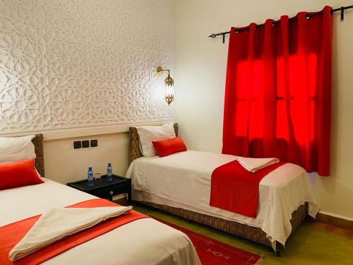 a bedroom with two beds with red curtains at Hotel Kasbah Ennakhile in Nkob