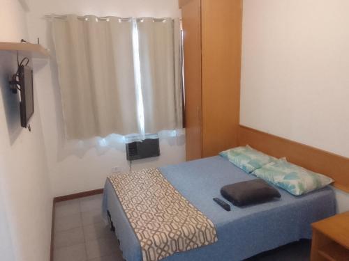 um pequeno quarto com uma cama azul e uma janela em Acomodação Cecília. em Campos dos Goytacazes
