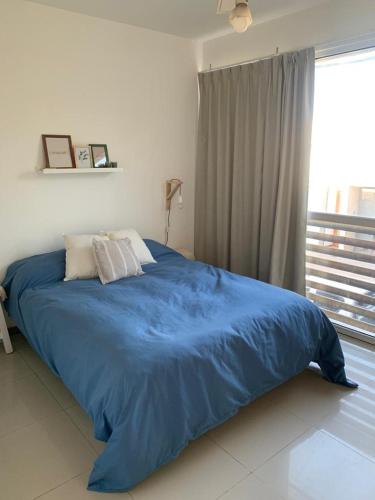 Cama azul en habitación blanca con ventana en Apartamento Paseo Plaza Navarro en Navarro