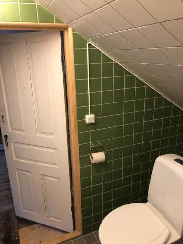 a bathroom with a toilet and a green tiled wall at Mysigt men trångt vindsrum i Svinaberga! in Kivik
