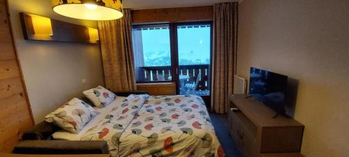 een slaapkamer met een bed, een televisie en een raam bij Lune D'Argent Appartement avec vue sur la montagne in Megève