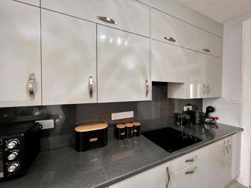 a kitchen with white cabinets and a black counter top at Anchorage, a lovely 2nd floor one bedroom apartment with fabulous seaviews in Largs