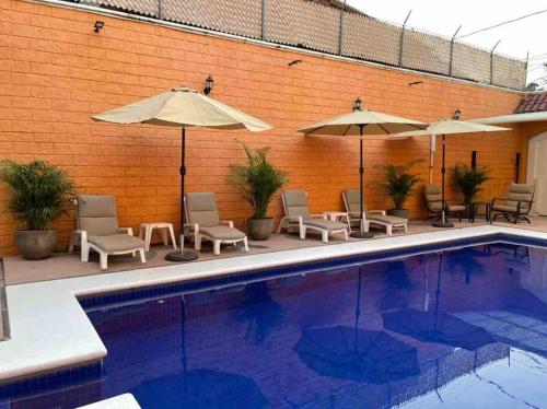 a swimming pool with chairs and umbrellas next to a brick wall at Erase una vez o la Catarina in Zihuatanejo