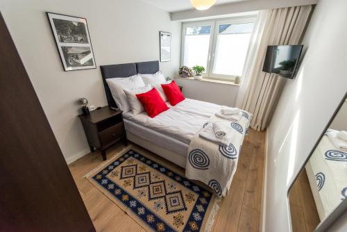 um pequeno quarto com uma cama com almofadas vermelhas e uma janela em Apartament Wilaneska em Krynica Zdrój