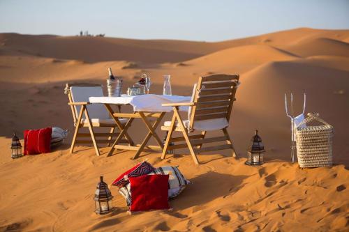 uma mesa e cadeiras na areia no deserto em Desert Queen Camp ( typical luxury) em Merzouga