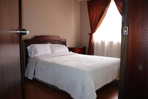 a bedroom with a bed with white sheets and a window at Cozy and Spacious Home with Incredible Location in Cuenca