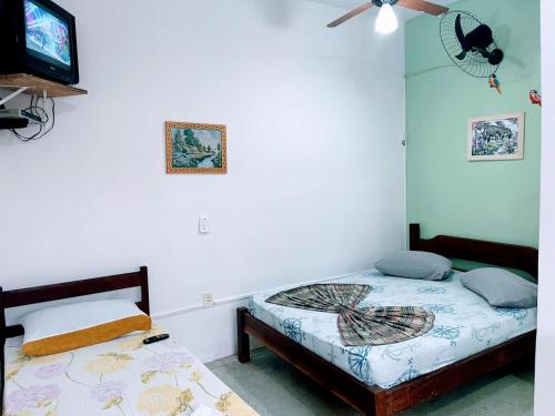 a bedroom with two beds and a tv on the wall at Pousada Nova Opção in Bertioga