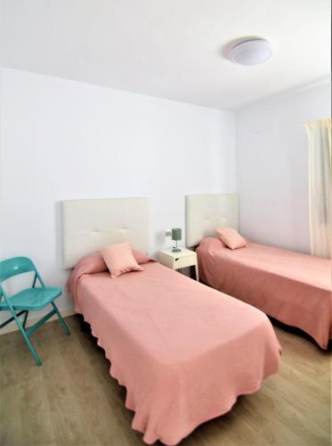a room with two beds with pink sheets and a chair at Apartamento Martina in Puerto del Carmen