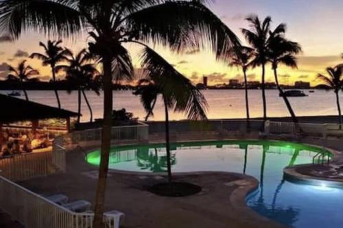 a swimming pool with palm trees in front of the ocean at Appartement spacieux au village du flamboyant in Baie Nettle